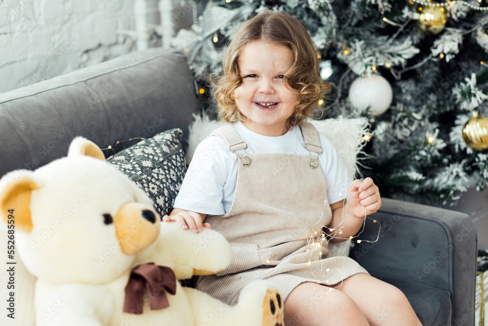 Cute little girl in a beautiful dress near decorated Christmas and new year tree at home with her teddy bear. Smiling, cheerful and happy Cute little girl in a beautiful dress near decorated Christmas and new year tree at home with her teddy bear. Smiling, cheerful and happy
