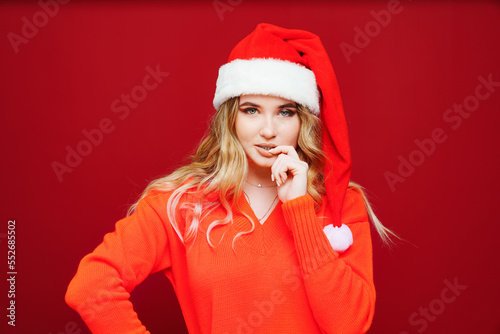 a thoughtful beautiful woman in a Santa Claus hat on a red background. 