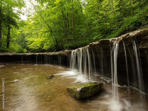 Small waterfalls flow over a ledge on an unnamed creek surrounded by lush green forests; Strathroy, Ontario, Canada photo