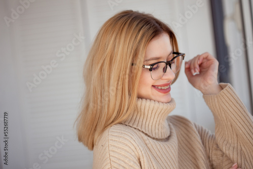 Young cute blonde with eyeglasses and a beige sweater. Stylish fashionable young woman. woman with glasses smiling