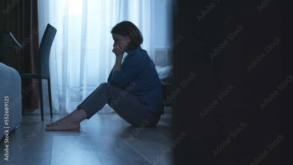 An unhappy woman sits on the floor near the bed. Sad and lonely woman, depression, mental health, relationship problems.