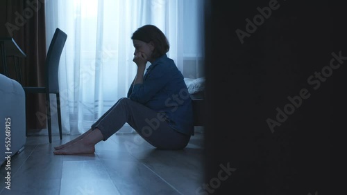 An unhappy woman sits on the floor near the bed. Sad and lonely woman, depression, mental health, relationship problems.