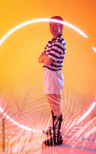 Confident caucasian female rugby player with arms crossed standing by illuminated plants and circle