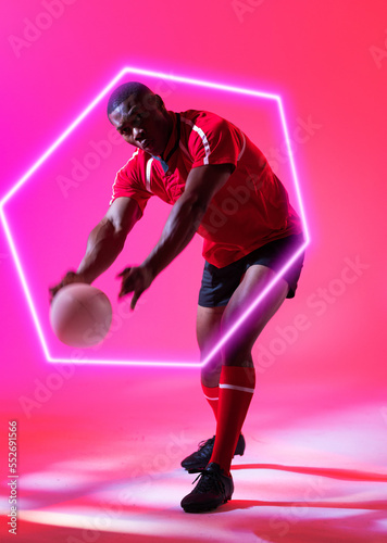 African american male player throwing rugby ball by illuminated hexagon over pink background