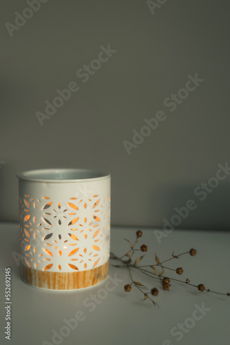 An aroma lamp, a candle holder for aromatic oils with a lit candle, stands on a table against a gray wall. Minimalism with a sprig of dried flowers photo