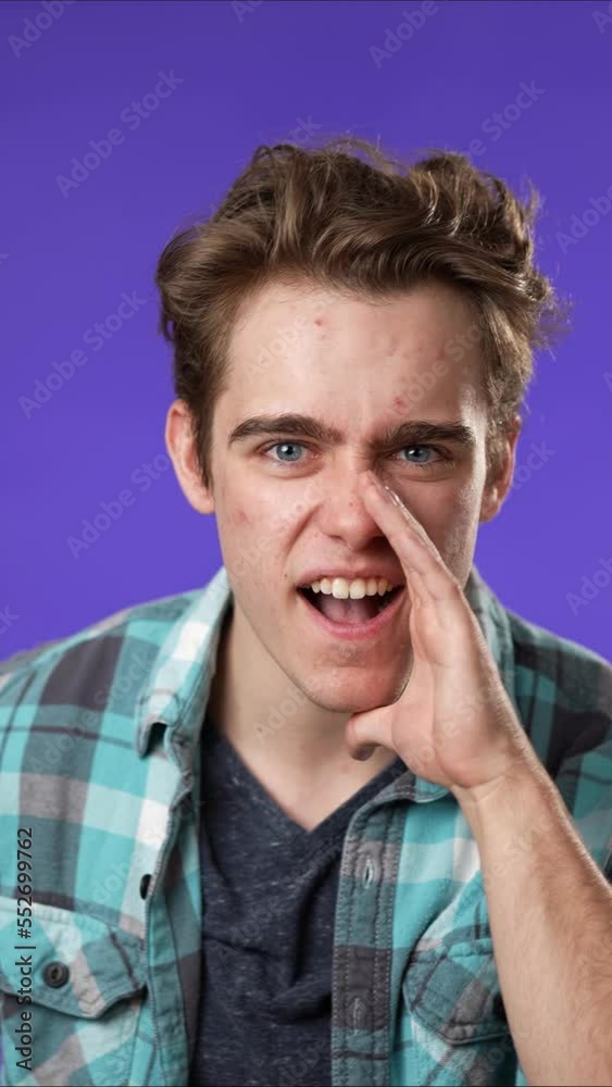 Vertical video portrait of caucasian hipster man 20s looks around put hand to mouth tells secret isolated on purple background studio portrait Vertical video portrait of caucasian hipster man 20s looks around put hand to mouth tells secret isolated on purple background studio portrait
