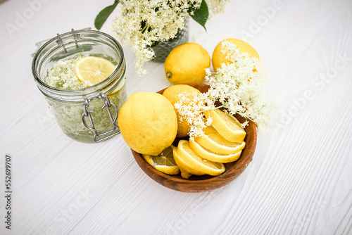 A wooden plate with fresh lemons for a healthy refreshing non-alcoholic lemonade with syrup from elderflower flowers. Still life with freshly cut elderberry flowers in a jar. photo