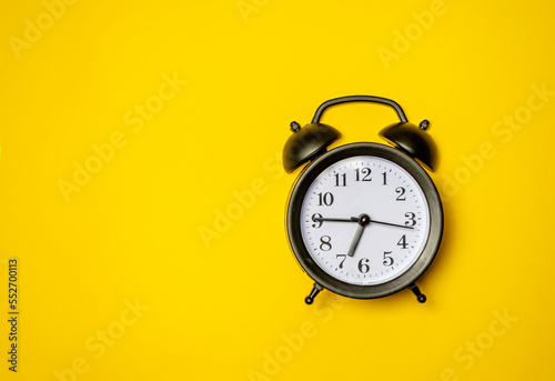 Black retro alarm clock on yellow background top view Flat lay