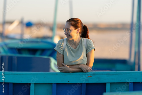 A woman stands in the port and leans her forearms into blue planks - looks to the side