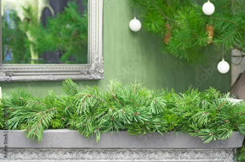 Gray fireplace with decorative mirror, decorated with fir branches.Beautiful green Christmas background
