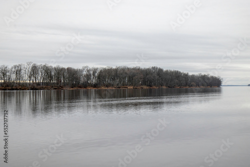 View across a calm river at a treed island, sky and trees reflected in water, nobody
