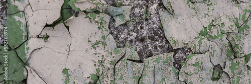 Peeling paint on the wall. Panorama of a concrete wall with old cracked flaking paint. Weathered rough painted surface with patterns of cracks and peeling. Wide panoramic grunge texture for background