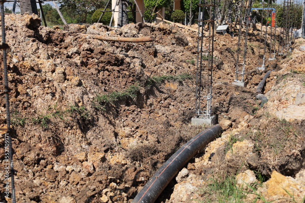 Frame of metal fence posts on a concrete base. Steel columns on concrete column base in trench of newly constructed outdoor fence on dark brown soil background with copy space with selective focus. Frame of metal fence posts on a concrete base. Steel columns on concrete column base in trench of newly constructed outdoor fence on dark brown soil background with copy space with selective focus.