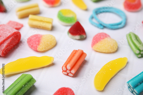 Many tasty colorful jelly candies on white tiled table, closeup