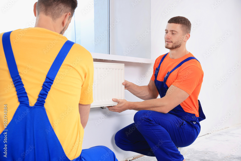 Obraz premium Professional plumbers installing new heating radiator in room