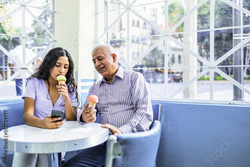 Teen girl and her grandfather using mobile phone in ice cream shop.