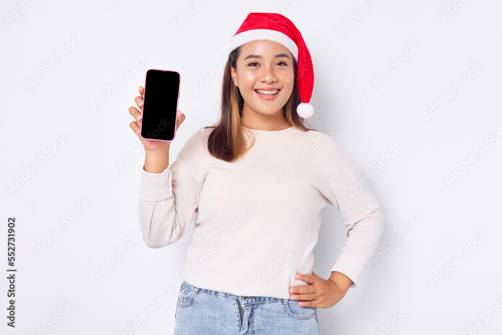 Smiling young Asian woman in a Christmas hat showing blank screen mobile phone isolated on white background Smiling young Asian woman in a Christmas hat showing blank screen mobile phone isolated on white background