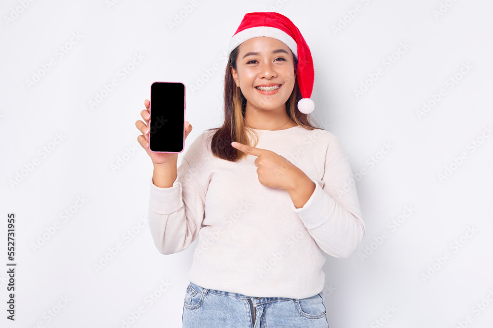 Smiling young Asian woman in a Christmas hat showing blank screen mobile phone, recommending mobile app isolated on white background Smiling young Asian woman in a Christmas hat showing blank screen mobile phone, recommending mobile app isolated on white background