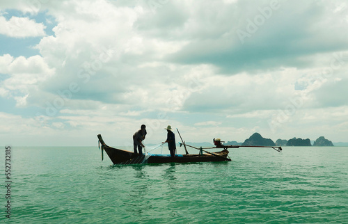 Thai fishermen catch fish with a net, traditional fishing in Thailand, fishing boat and fishermen on the background of tropical forests © maxa0109