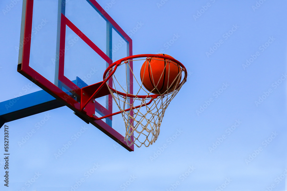 The sport of basketball. A basketball in a basket on an outdoor basketball court