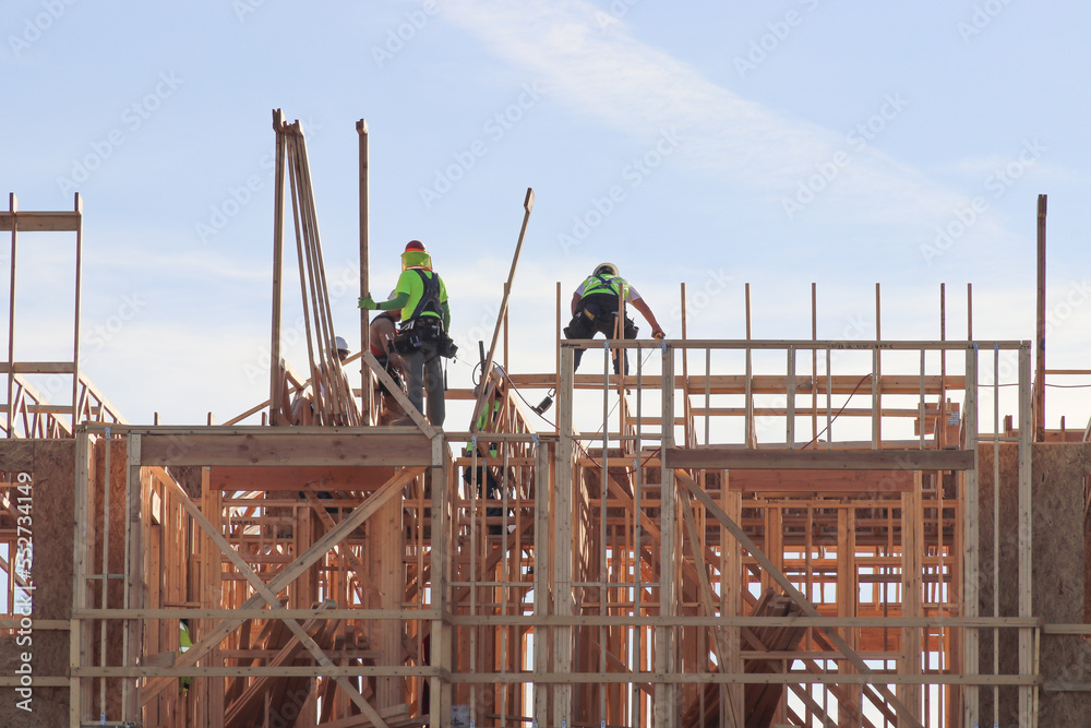 Crew of wood framing workers on top of structure of apartment building under construction