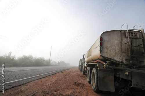 Construction water trucks parked along suburban road under foggy weather
