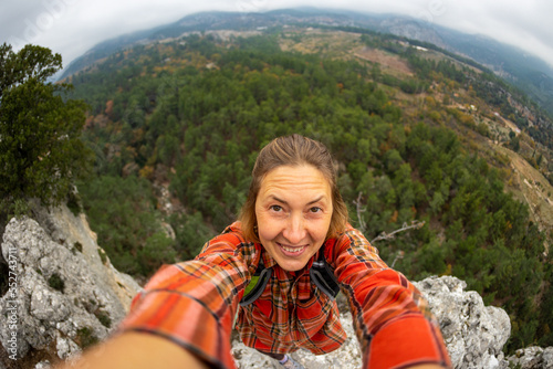 female tourist taking a selfie portrait on top of a mountain - Happy smiling woman using her smartphone - Hiking and rock climbing.