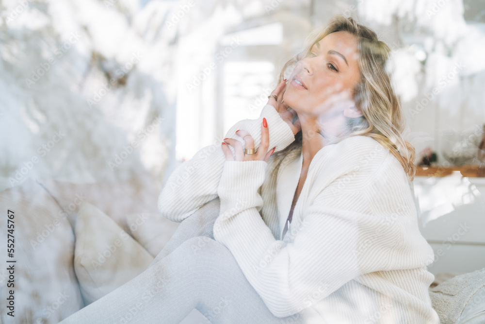 Young woman in white cardigan looking at window with winter landscape at home Young woman in white cardigan looking at window with winter landscape at home
