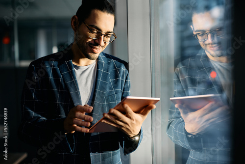 Happy Hispanic entrepreneur using touchpad by widow in office. photo