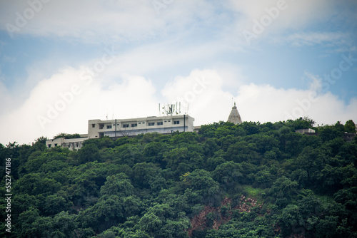 Concrete building with temple spire on top peak of aravalli range in jaipur against white monsoon clouds surrounded by green trees