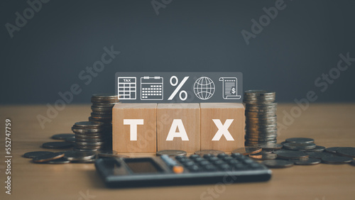 Financial planning concept or income and expenses, to show personal income tax, wooden block with TAX text, document icon above. and blurry rows of coins on table, business finance and banking