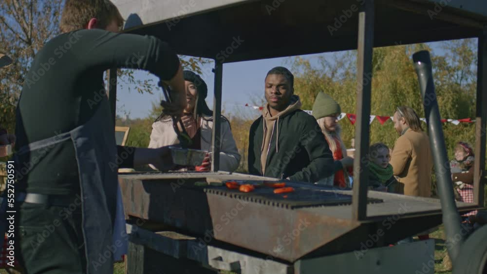 Multi ethnic family trying food cooked on grill. Adult man takes off ready to eat vegetables and put a portion on plate. Weekend on local farmers market. Multi ethnic family trying food cooked on grill. Adult man takes off ready to eat vegetables and put a portion on plate. Weekend on local farmers market.