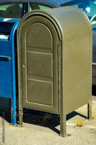 Green mail box in urban area of the city downtown with round top and square body near a blue canister