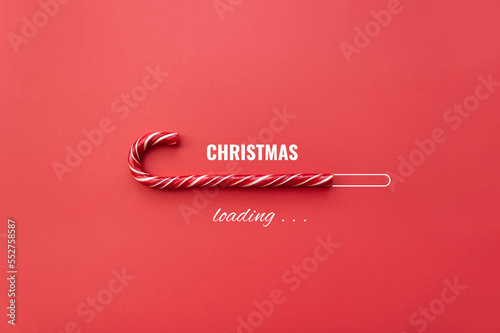 Striped candy cane and lettering Christmas loading on red background. Concept of waiting for seasonal holidays. Copy space, selective focus