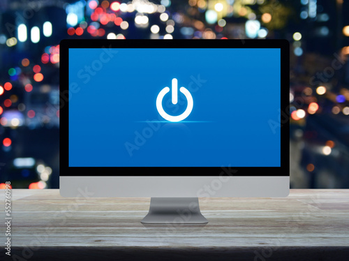 Power button icon on desktop modern computer monitor screen on wooden table over blur colorful night light traffic jam road in city, Business start up online concept