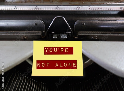Vintage typewriter with yellow stick note written YOU'RE NOT ALONE - Concept of positive self talk or affirmation, encouragement message  to support other people when life seems difficult and hopeless
