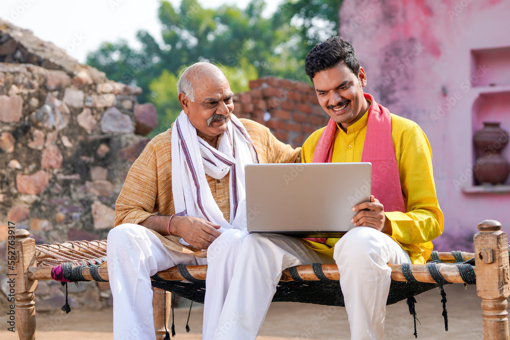 Young indian farmer showing some detail to his father in laptop.