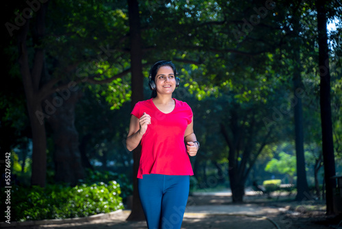 Fototapeta Naklejka Na Ścianę i Meble -  young indian woman with earphones listening music during jogging at park.