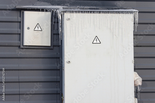 Frozen and covered with ice and icicles fuse box installed outside on the wall of a building