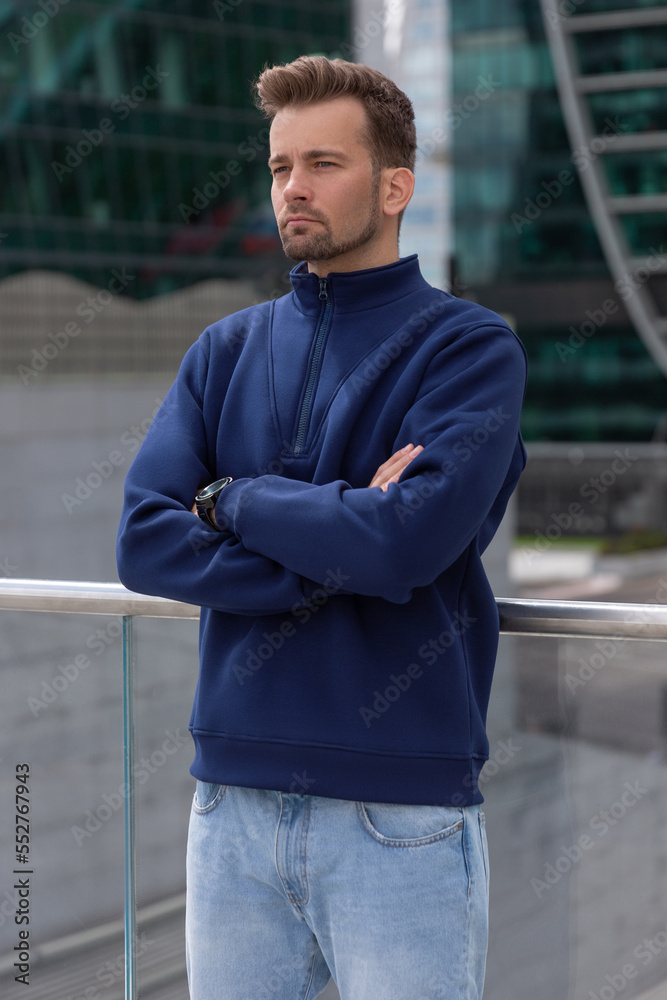 City portrait of handsome hipster guy with beard wearing blue blank hoodie or sweatshirt with space for your logo or design. Mockup for print