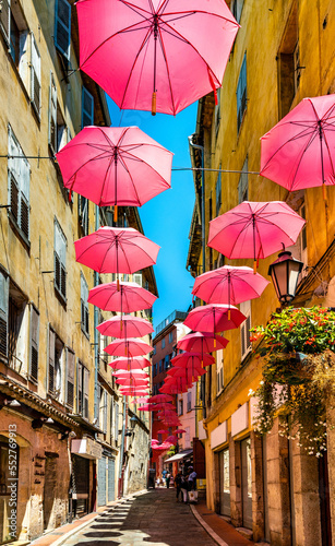Historic tenement houses and narrow streets decorated with pink umbrellas of old town quarter of perfumery city of Grasse in south France