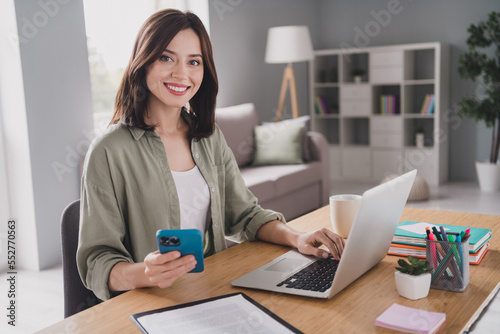 Photo of joyful pretty charming successful lady boss ceo sitting table using modern gadgets macbook iphone indoors room workstation