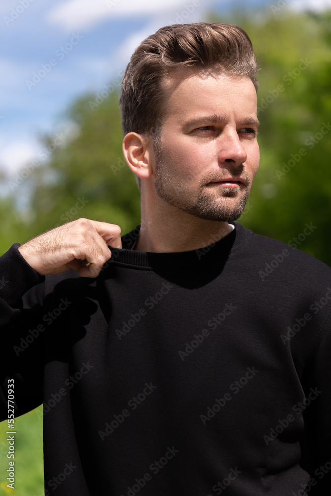 City portrait of handsome hipster guy with beard wearing black blank hoodie or sweatshirt with space for your logo or design. Mockup for print