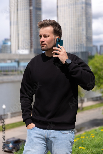 Obraz na płótnie City portrait of handsome hipster guy with beard wearing black blank hoodie or sweatshirt with space for your logo or design. Talking on the phone. Mockup for print w salonie