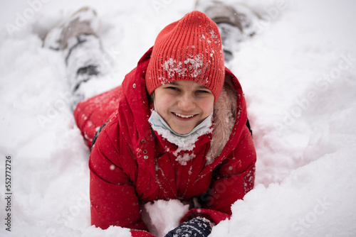 A girl in a red jacket in the snow. The girl smiles and lies on the snow. Winter fun.