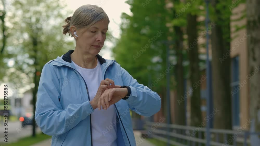 Sporty mature runner woman standing in the street using smart watch equipment app technology monitor active gadget jogger tech. Sport and healthy lifestyle concept. Aging Youthfully Sporty mature runner woman standing in the street using smart watch equipment app technology monitor active gadget jogger tech. Sport and healthy lifestyle concept. Aging Youthfully