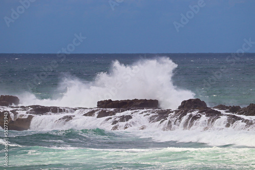 Waves crashing over the rocks near Fingal Bay, with a container or cargo ship in the background.