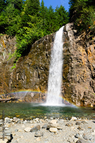 Waterfall surrounded by trees and rocks with a rainbow at the bottom
