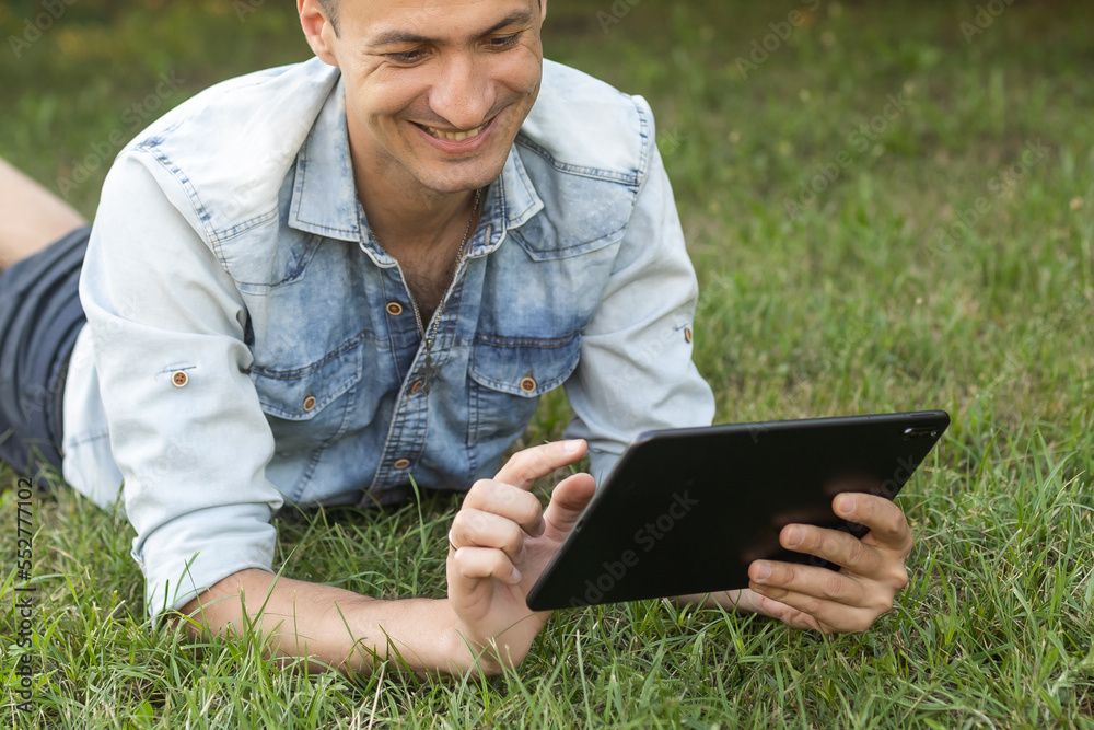 Young Man with a Tablet Computer on the Green Leaves Background outdoor. Young Man with a Tablet Computer on the Green Leaves Background outdoor.