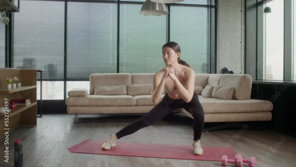 Young Sporty Asian Woman in sportswear doing fitness exercises. Female fitness practicing leg stretching exercises on yoga mat at home. Pretty lady burning calories, practice pilates. Healthcare and